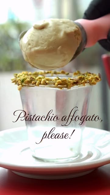Pistachio gelato being placed into a glass of espresso rimmed with crushed pistachio